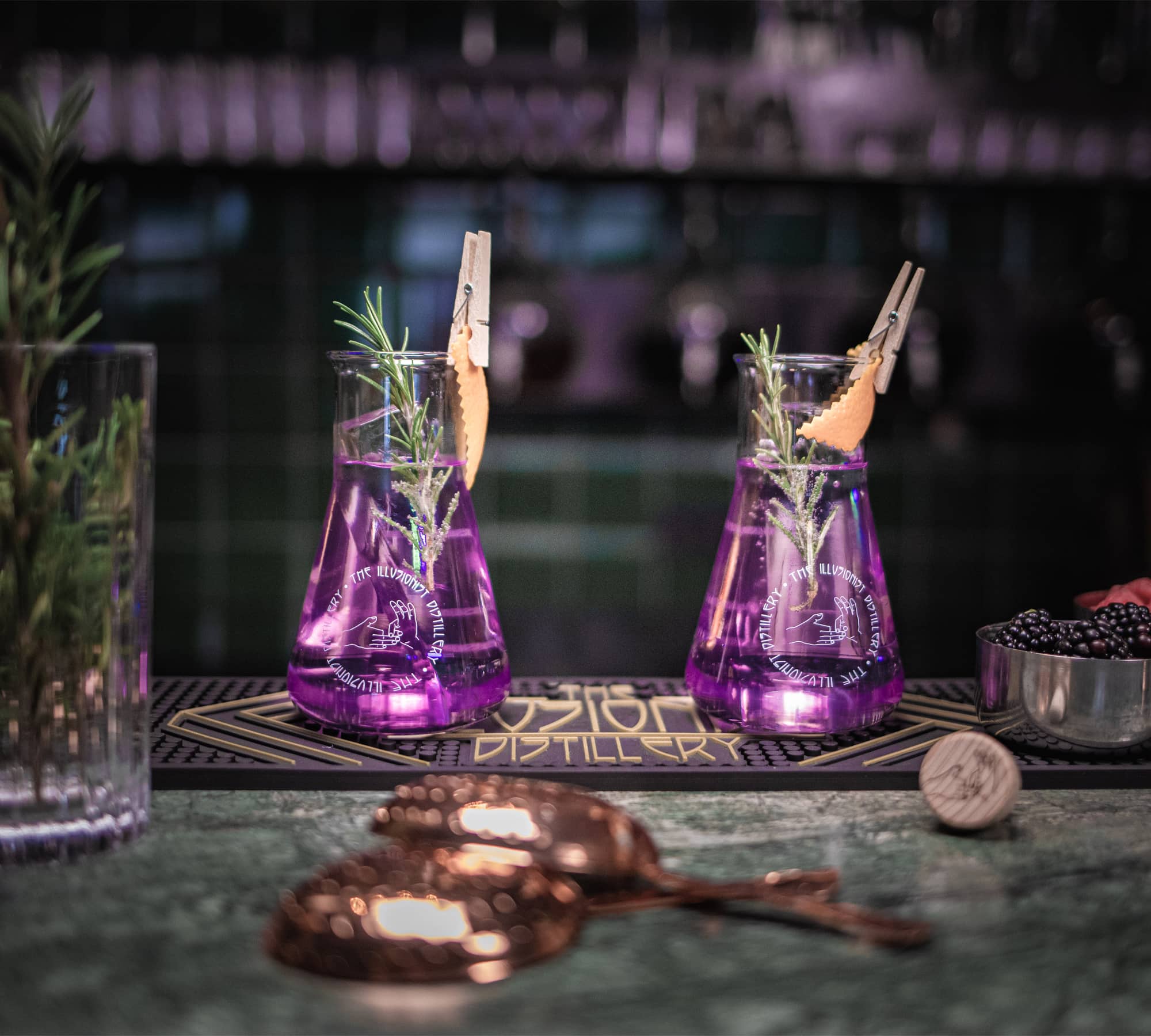 Focused photo on two served Illusionist Dry Gin glassware with purple gin.